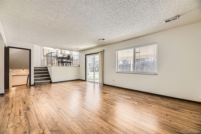unfurnished living room featuring a textured ceiling, visible vents, wood finished floors, and stairway