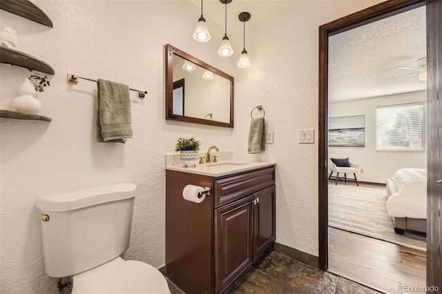 ensuite bathroom featuring toilet, vanity, a textured ceiling, connected bathroom, and baseboards