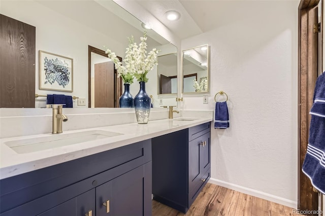 bathroom with baseboards, double vanity, a sink, and wood finished floors