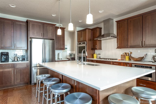 kitchen featuring wall chimney exhaust hood, a kitchen island with sink, and appliances with stainless steel finishes