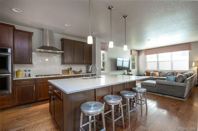 kitchen with wall chimney exhaust hood, a kitchen breakfast bar, sink, and a kitchen island with sink