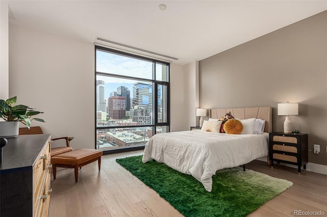 bedroom with expansive windows, light wood finished floors, a view of city, and baseboards