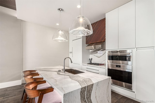 kitchen with appliances with stainless steel finishes, white cabinets, a sink, light stone countertops, and wall chimney exhaust hood