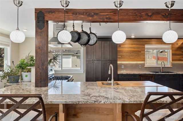 kitchen featuring wall chimney range hood, plenty of natural light, a sink, and tasteful backsplash