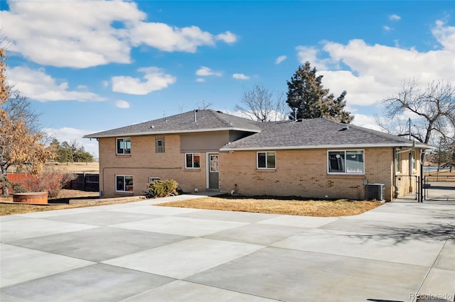 rear view of house featuring brick siding, a shingled roof, a gate, central AC, and fence