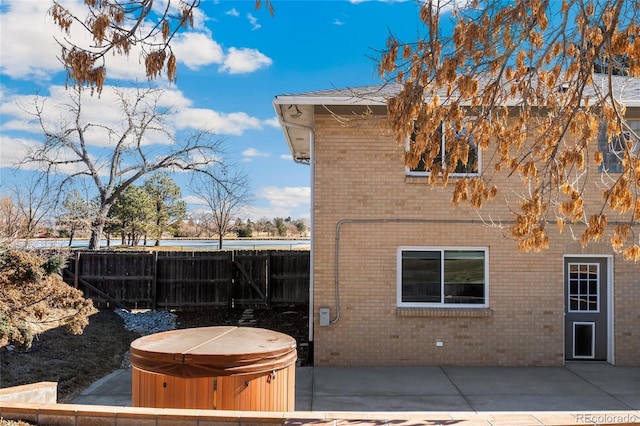 view of property exterior with a patio area, a hot tub, fence, and brick siding