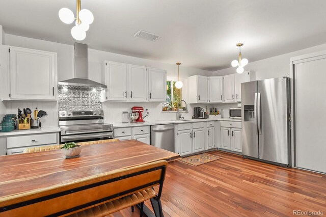 4040 Cody St, Wheat Ridge, CO 80033 - kitchen with stainless steel appliances, wall chimney range hood, decorative light fixtures, decorative backsplash, and light wood-style floors