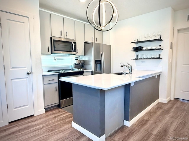 kitchen with appliances with stainless steel finishes, open shelves, a sink, a peninsula, and light wood-style floors