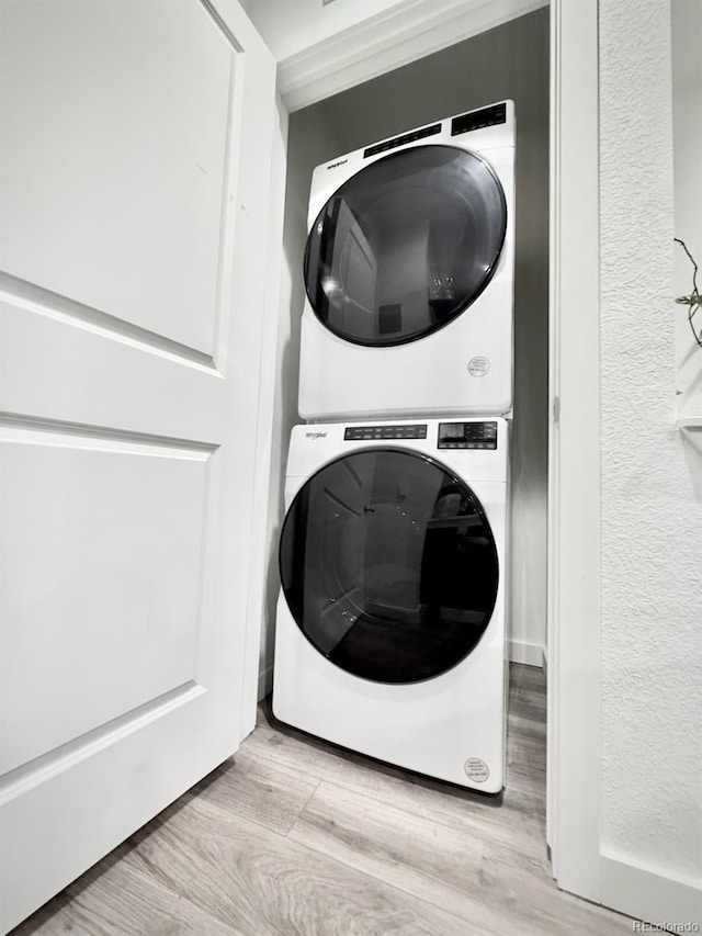 laundry area with stacked washer / drying machine, a textured wall, wood finished floors, and laundry area