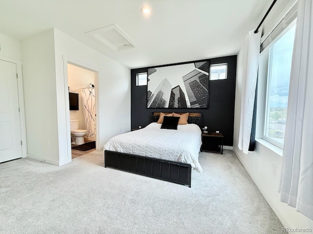 bedroom featuring baseboards, light colored carpet, ensuite bathroom, and attic access
