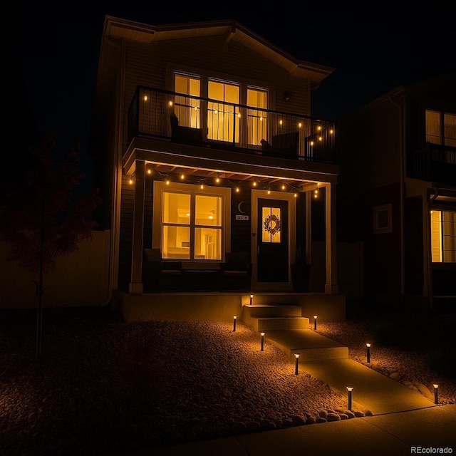 back of house at twilight featuring a porch and a balcony