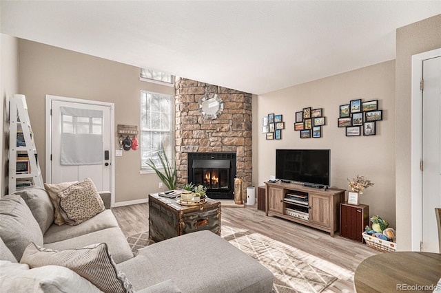 living room with lofted ceiling, a stone fireplace, and light hardwood / wood-style floors