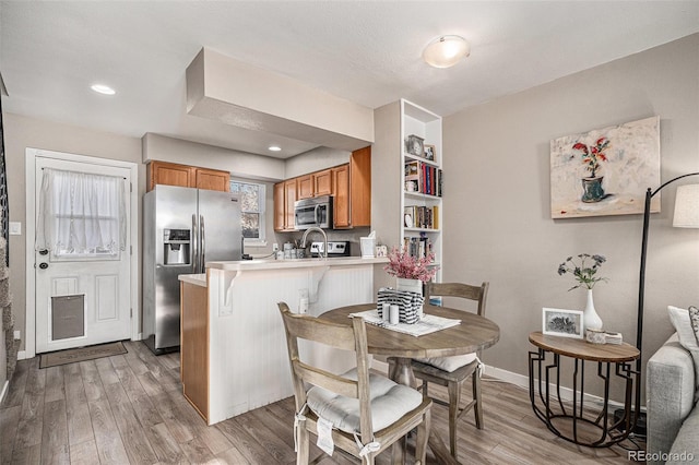 kitchen featuring built in features, a kitchen bar, light hardwood / wood-style floors, kitchen peninsula, and stainless steel appliances