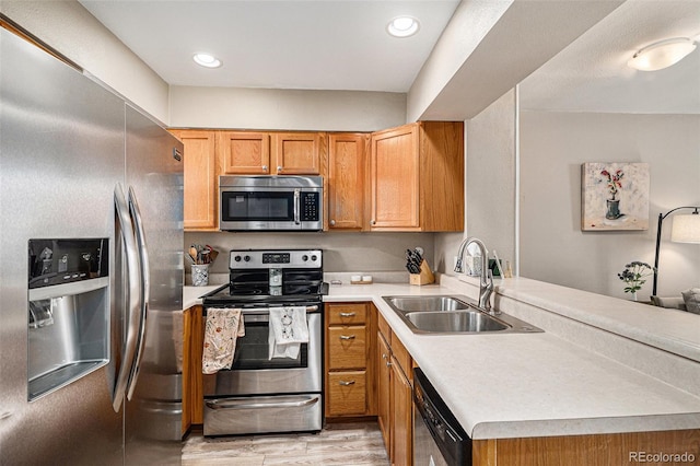 kitchen featuring appliances with stainless steel finishes, sink, light hardwood / wood-style floors, and kitchen peninsula