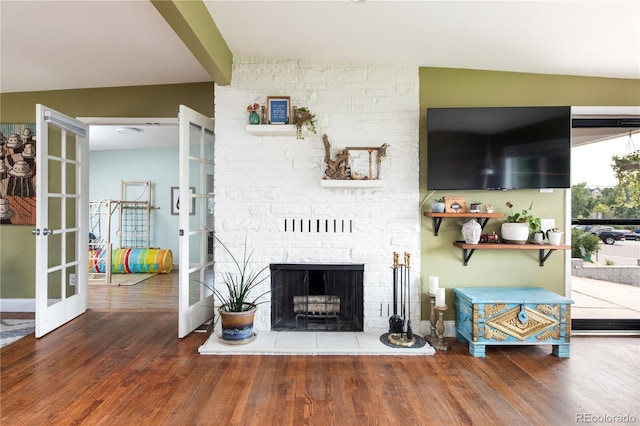 living room with a brick fireplace, hardwood / wood-style floors, french doors, and vaulted ceiling with beams