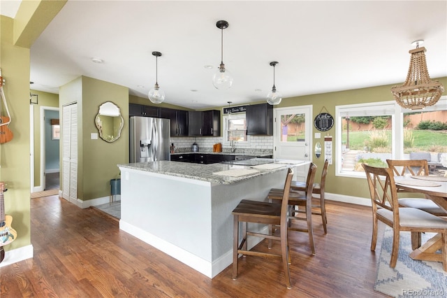 kitchen featuring stainless steel refrigerator with ice dispenser, decorative light fixtures, backsplash, and light stone countertops