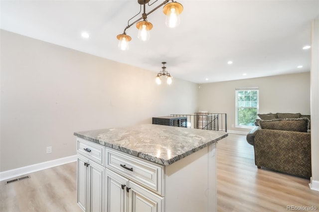 kitchen with light wood-style floors, a kitchen island, baseboards, decorative light fixtures, and light stone countertops