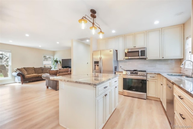 kitchen featuring appliances with stainless steel finishes, a sink, light wood-style flooring, cream cabinetry, and light stone counters