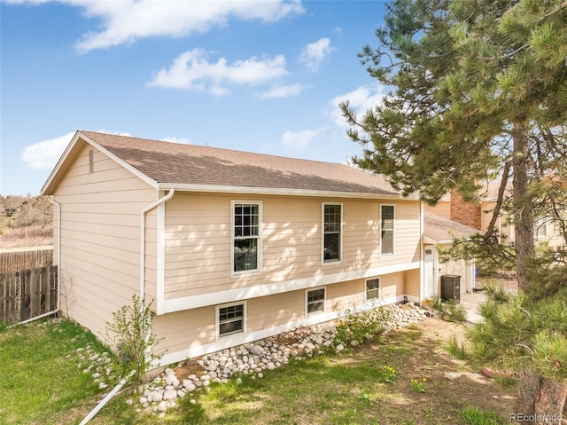 view of side of home with fence, cooling unit, and a shingled roof