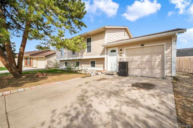 split level home featuring a garage, concrete driveway, and fence