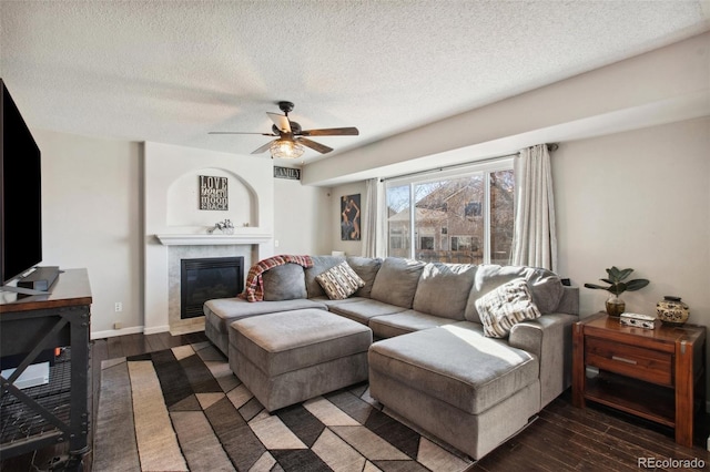 living room featuring a textured ceiling, a fireplace, ceiling fan, and dark wood-type flooring