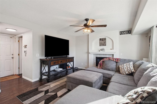 living room featuring ceiling fan, a fireplace, dark hardwood / wood-style flooring, and a textured ceiling