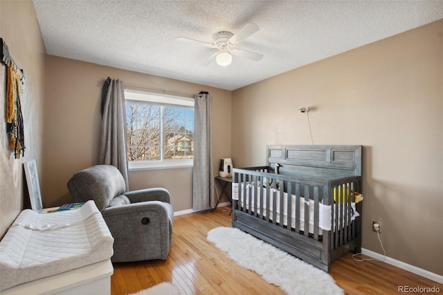 bedroom featuring ceiling fan, a nursery area, a textured ceiling, and light wood-type flooring