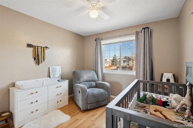 bedroom featuring a textured ceiling, light wood-type flooring, a nursery area, and ceiling fan