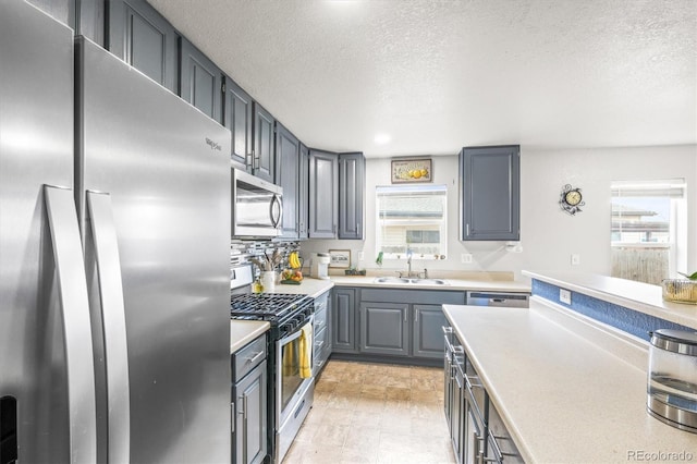 kitchen featuring backsplash, sink, gray cabinets, a textured ceiling, and appliances with stainless steel finishes