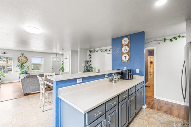 kitchen with blue cabinetry, kitchen peninsula, stainless steel fridge, a textured ceiling, and a breakfast bar