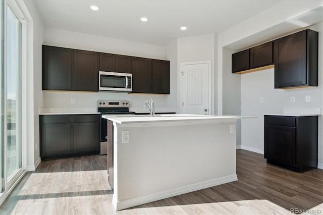 kitchen with dark brown cabinetry, stainless steel appliances, dark hardwood / wood-style floors, and an island with sink