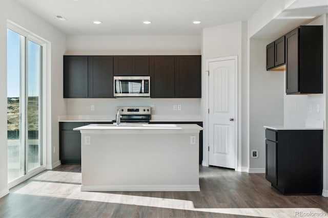 kitchen with stainless steel appliances, hardwood / wood-style floors, dark brown cabinets, and a center island with sink