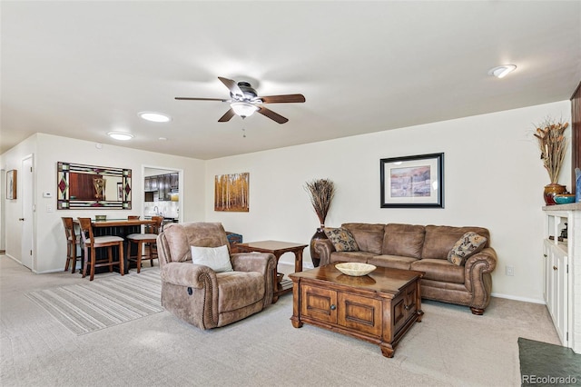 living area featuring baseboards, a ceiling fan, and light colored carpet