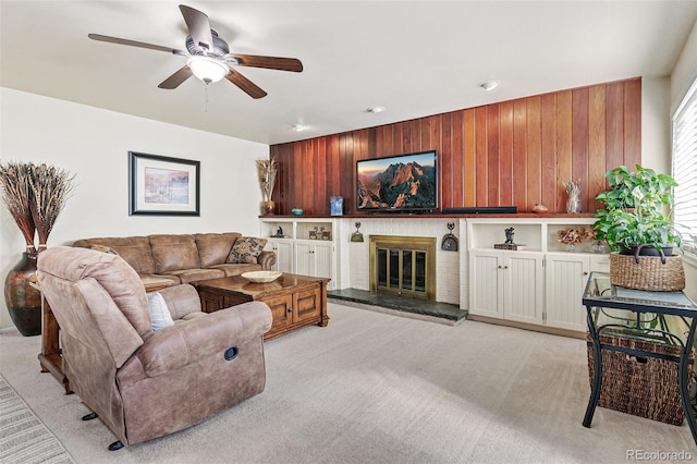 living room featuring a brick fireplace, ceiling fan, light colored carpet, and wood walls