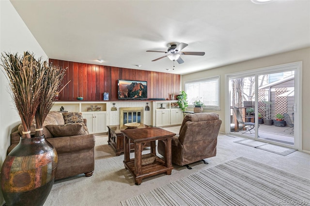 living room featuring a brick fireplace, light carpet, ceiling fan, and wooden walls