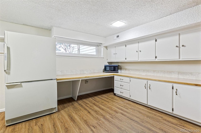 kitchen with white cabinets, light wood-style floors, light countertops, built in study area, and freestanding refrigerator