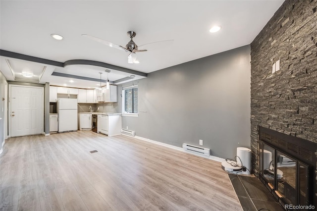 unfurnished living room with ceiling fan, light wood-style flooring, baseboard heating, and a stone fireplace