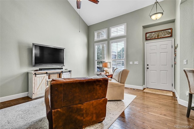 living room featuring a ceiling fan, high vaulted ceiling, baseboards, and hardwood / wood-style floors