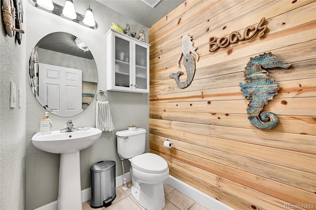 bathroom with baseboards, tile patterned flooring, a textured wall, and toilet