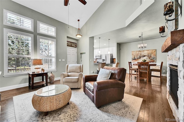 living area featuring a ceiling fan, a towering ceiling, a fireplace, dark wood finished floors, and baseboards