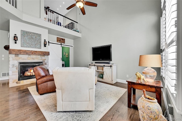 living area featuring visible vents, baseboards, ceiling fan, a high ceiling, and a barn door