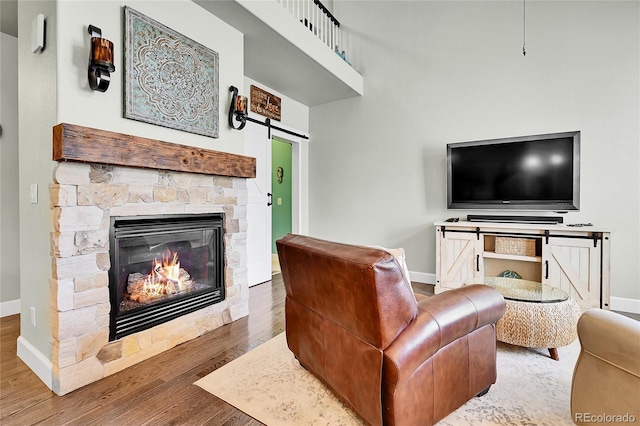 living room featuring baseboards, a barn door, wood finished floors, and a stone fireplace