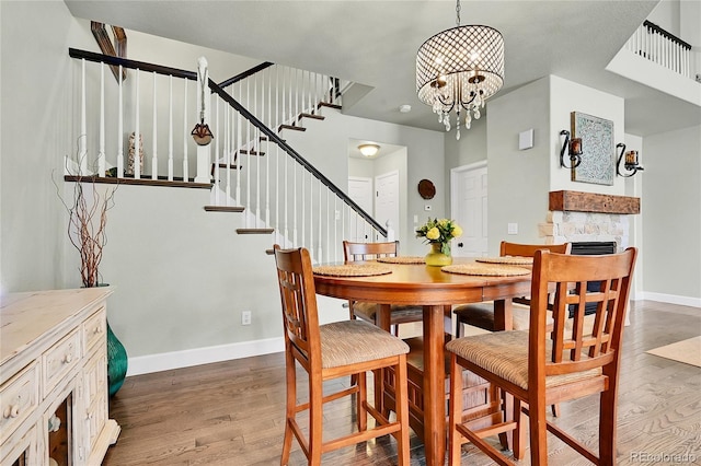 dining room featuring baseboards, a stone fireplace, stairs, and wood finished floors