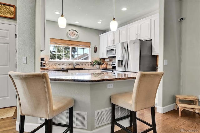 kitchen featuring a breakfast bar, white cabinets, a sink, light wood finished floors, and stainless steel appliances