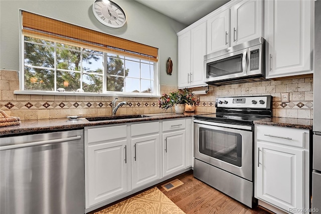 kitchen with a sink, stainless steel appliances, white cabinetry, wood finished floors, and visible vents