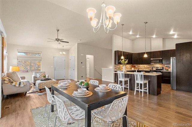 dining room with light hardwood / wood-style floors, ceiling fan with notable chandelier, and vaulted ceiling