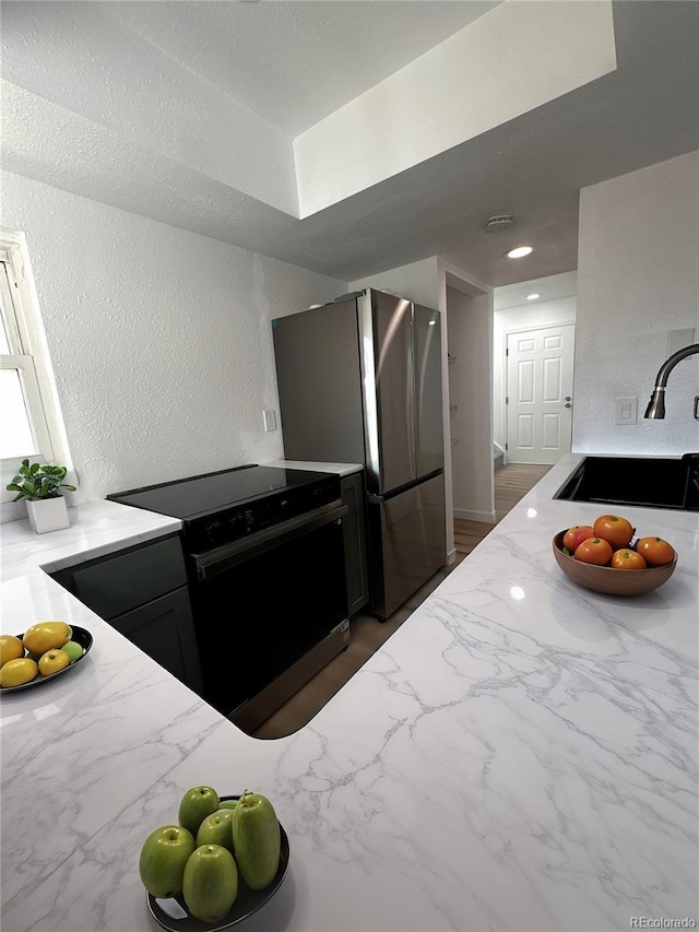 kitchen featuring a textured wall, light stone counters, electric range, a sink, and freestanding refrigerator