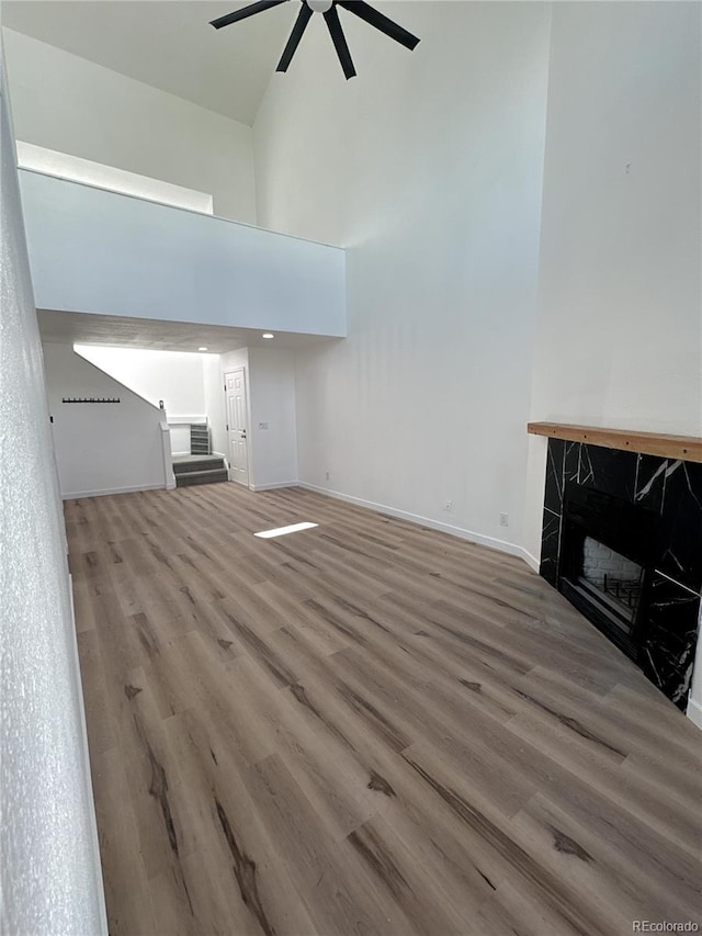 living room featuring stairway, a towering ceiling, ceiling fan, wood finished floors, and baseboards