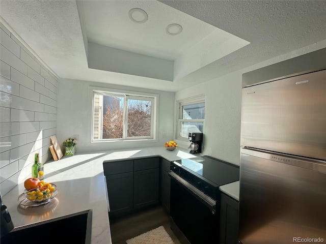 kitchen with electric stove, light countertops, backsplash, stainless steel refrigerator, and a tray ceiling