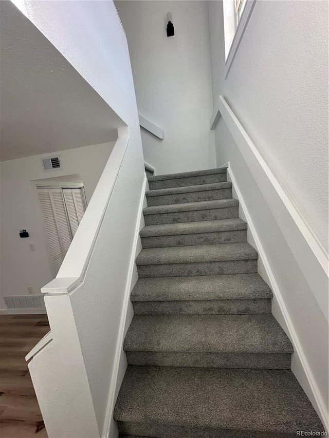 stairs with wood finished floors, visible vents, and baseboards